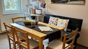 Un comedor con una mesa de madera, cuatro sillas, un sofá negro y un cuadro de una flor en la pared.