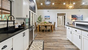 Une cuisine moderne avec des meubles blancs, un plan de travail noir et un plafond en bois.