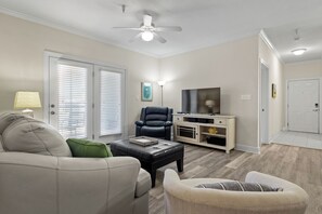 Una sala de estar con sofá, sillón, reposapiés, mueble para televisor y ventilador de techo.
