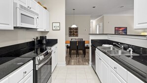 A modern kitchen with white cabinetry, a black countertop, and a dining area with a wooden table and chairs. - Fabulous Foley near the beach, ball fields, & OWA (Foley)