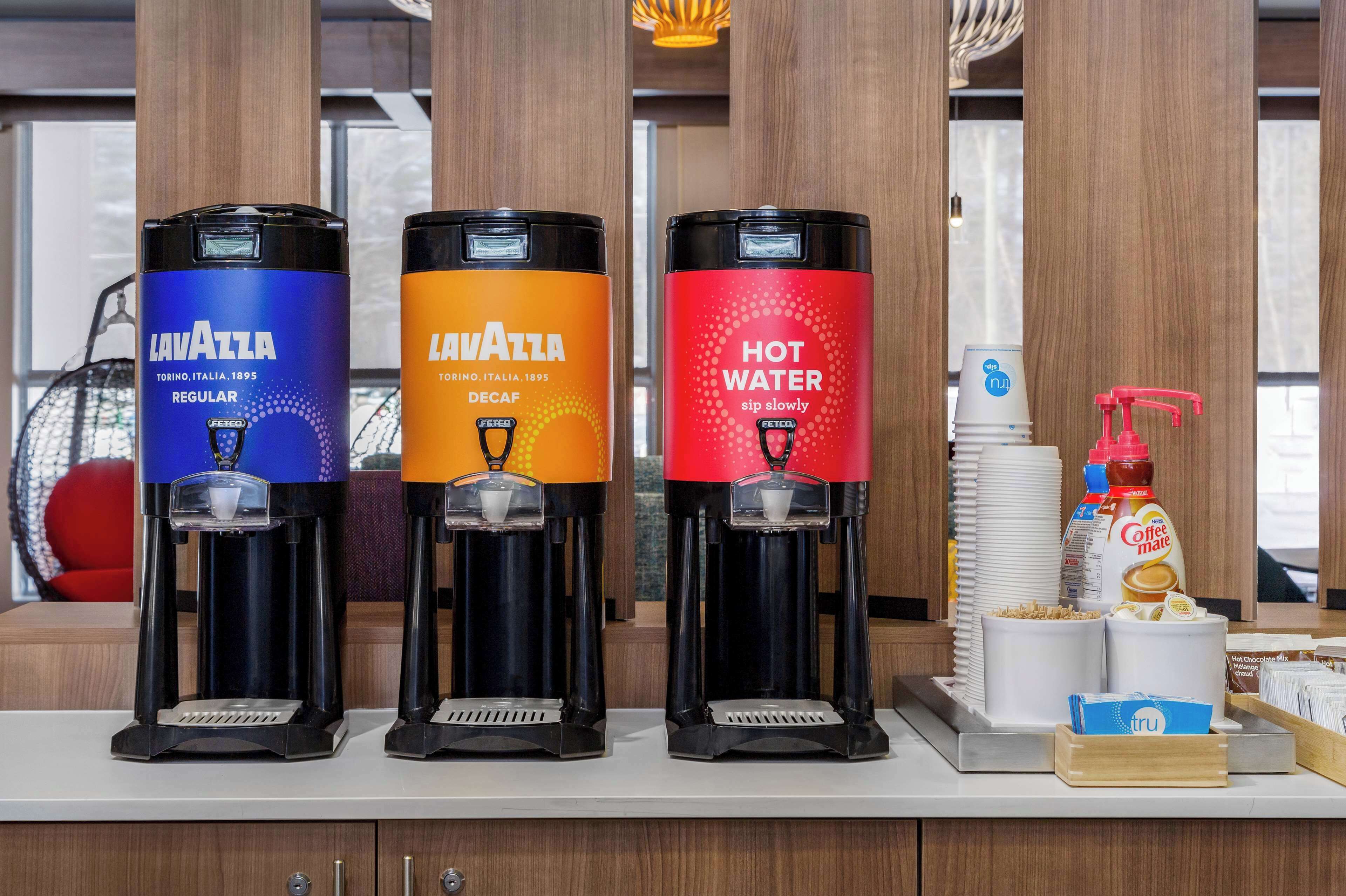 Trois distributeurs de café de la marque « Lavazza », proposant différentes options de boissons : café normal, café décaféiné et eau chaude.