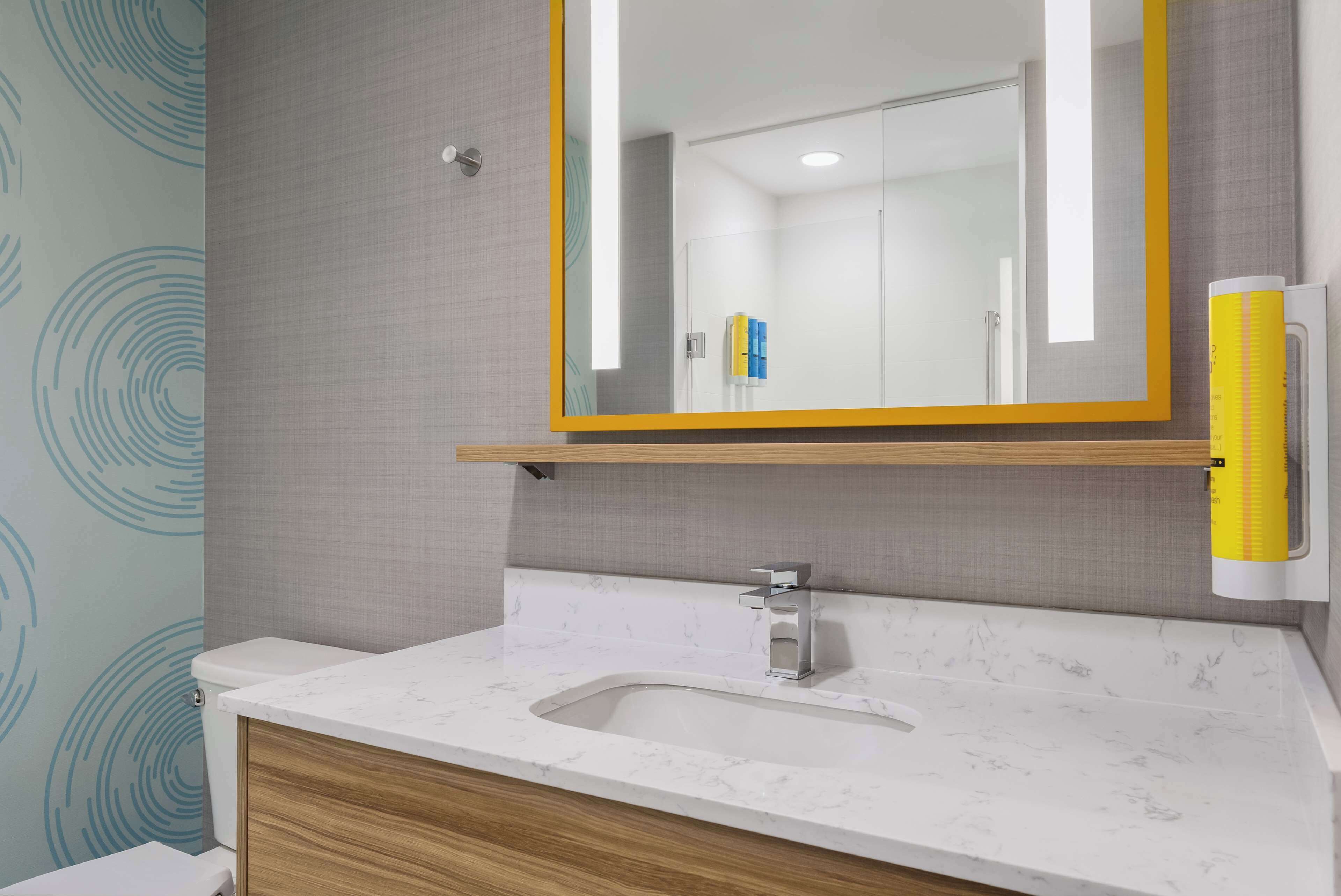 Un baño con lavamanos de mármol, tocador de madera y espejo con marco amarillo.