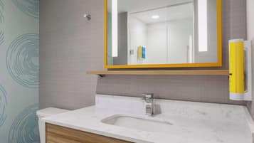 Un baño con lavamanos de mármol, tocador de madera y espejo con marco amarillo.