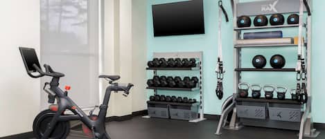 A gym with a stationary bike, dumbbells, kettlebells, and a TV on the wall.