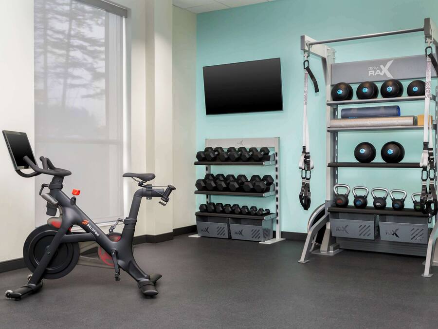 A gym with a stationary bike, dumbbells, kettlebells, and a TV on the wall.