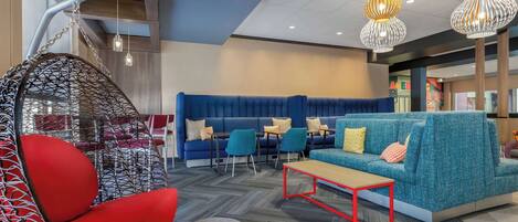 A modern lounge area with a blue sofa, red hanging chair, and a wooden coffee table.