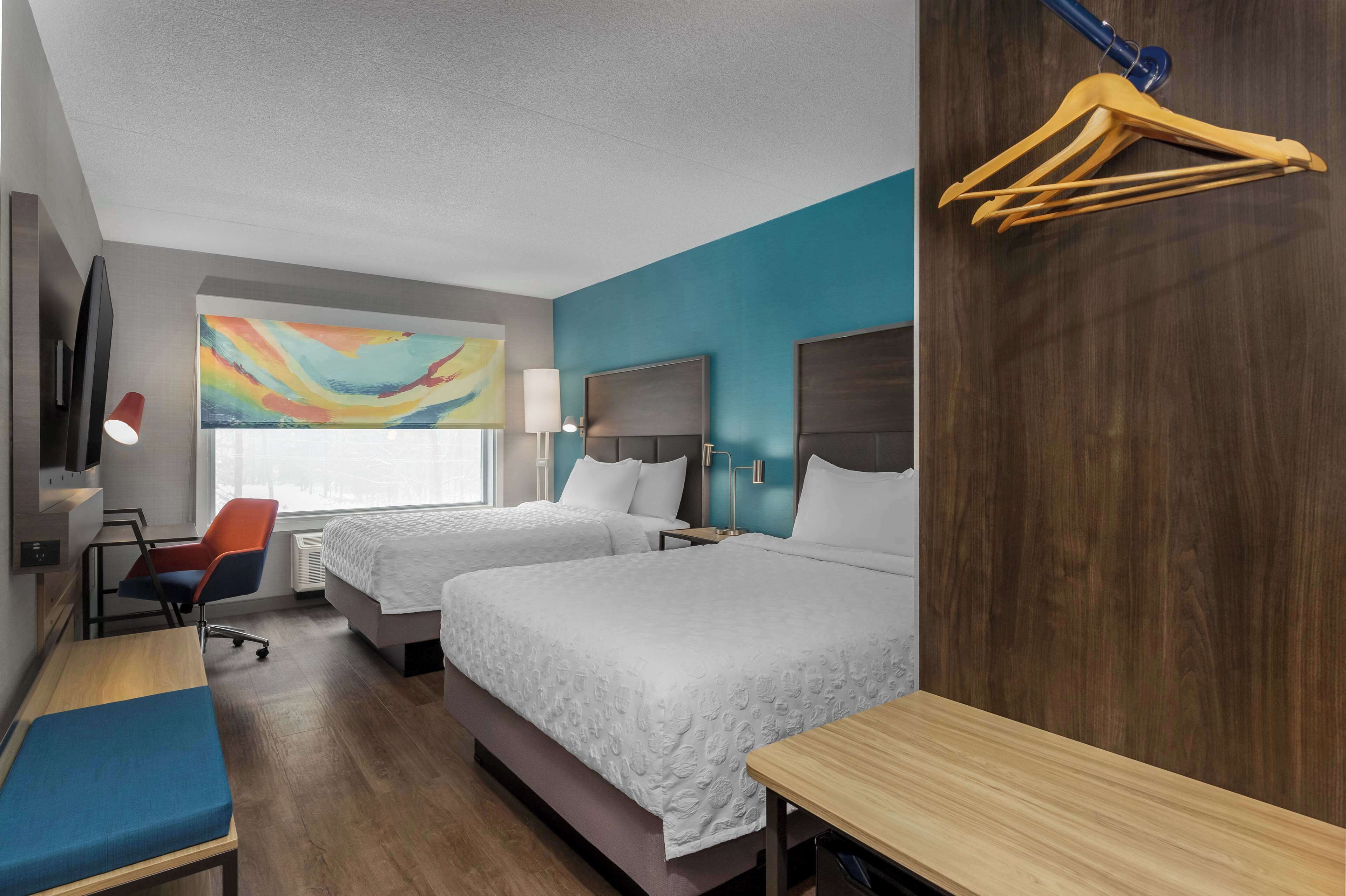 A hotel room with two beds, a desk, a chair, a TV, and a painting on the wall.