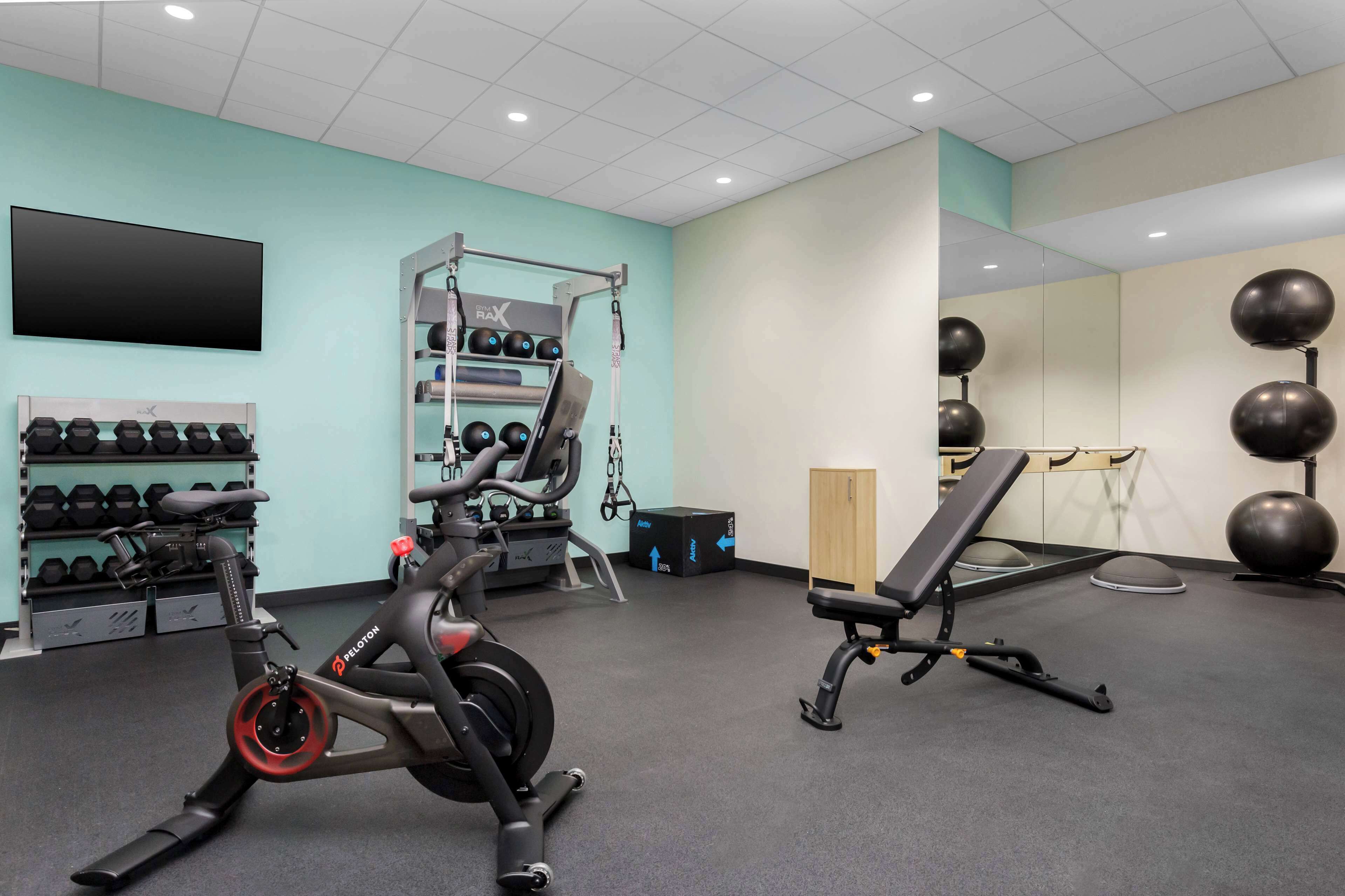 A gym with exercise equipment, a wall-mounted TV, and a mirror.