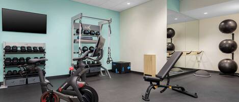 A gym with exercise equipment, a wall-mounted TV, and a mirror.