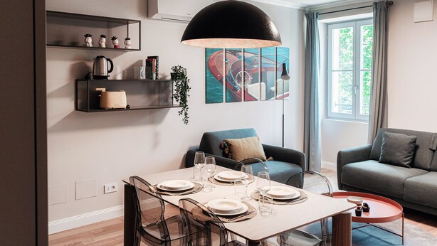 A modern living room with a dining area, a grey sofa, a coffee table, and a large window with curtains. - Marinetti Suite 7 (Como)