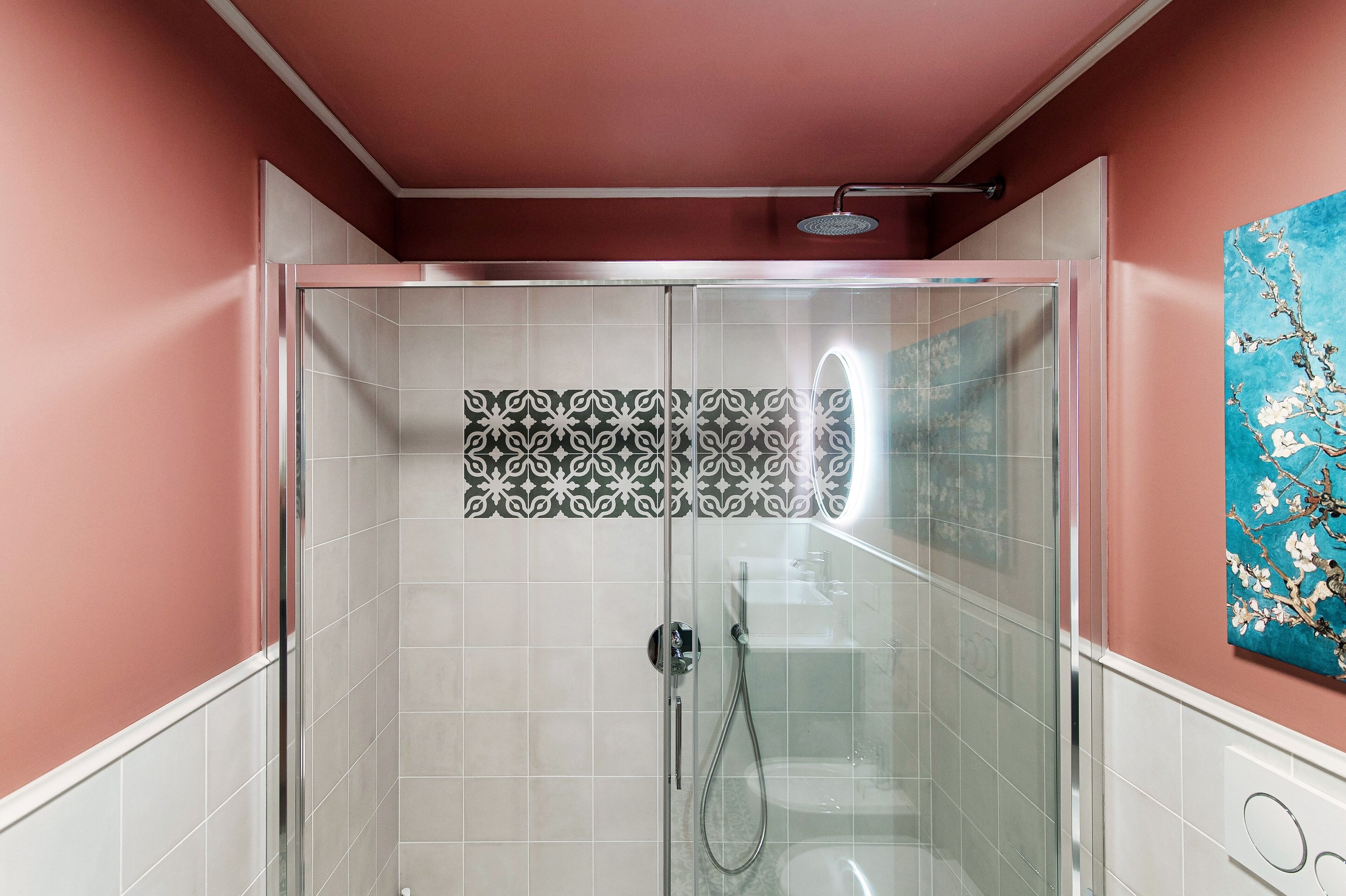 Una ducha envuelta en vidrio con pared de azulejos estampados, un cabezal de ducha de mano y un cabezal de ducha empotrado en el techo.