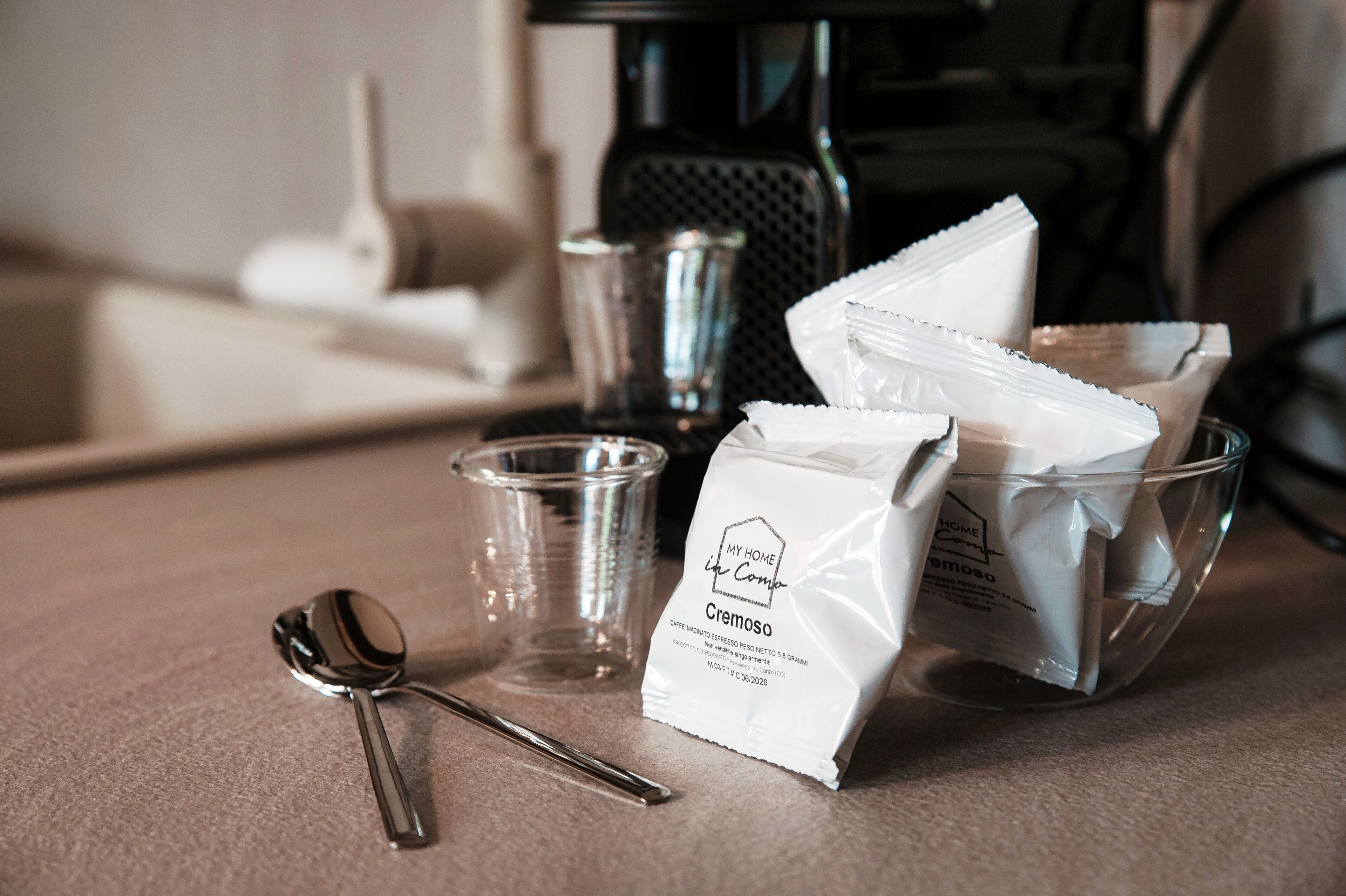 A kitchen counter with a coffee maker, a glass, a spoon, and a bag of coffee creamer.