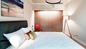 A bedroom with a bed, a red chair, a wardrobe, and a painting of a sailboat on the wall. - Marinetti Suite 7 (Como)