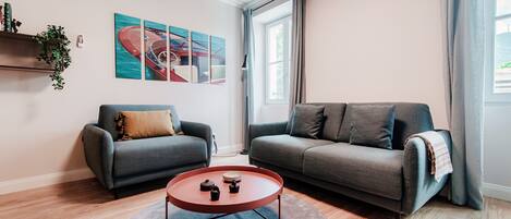 A modern living room with two grey sofas, a round coffee table, and a large window with curtains.