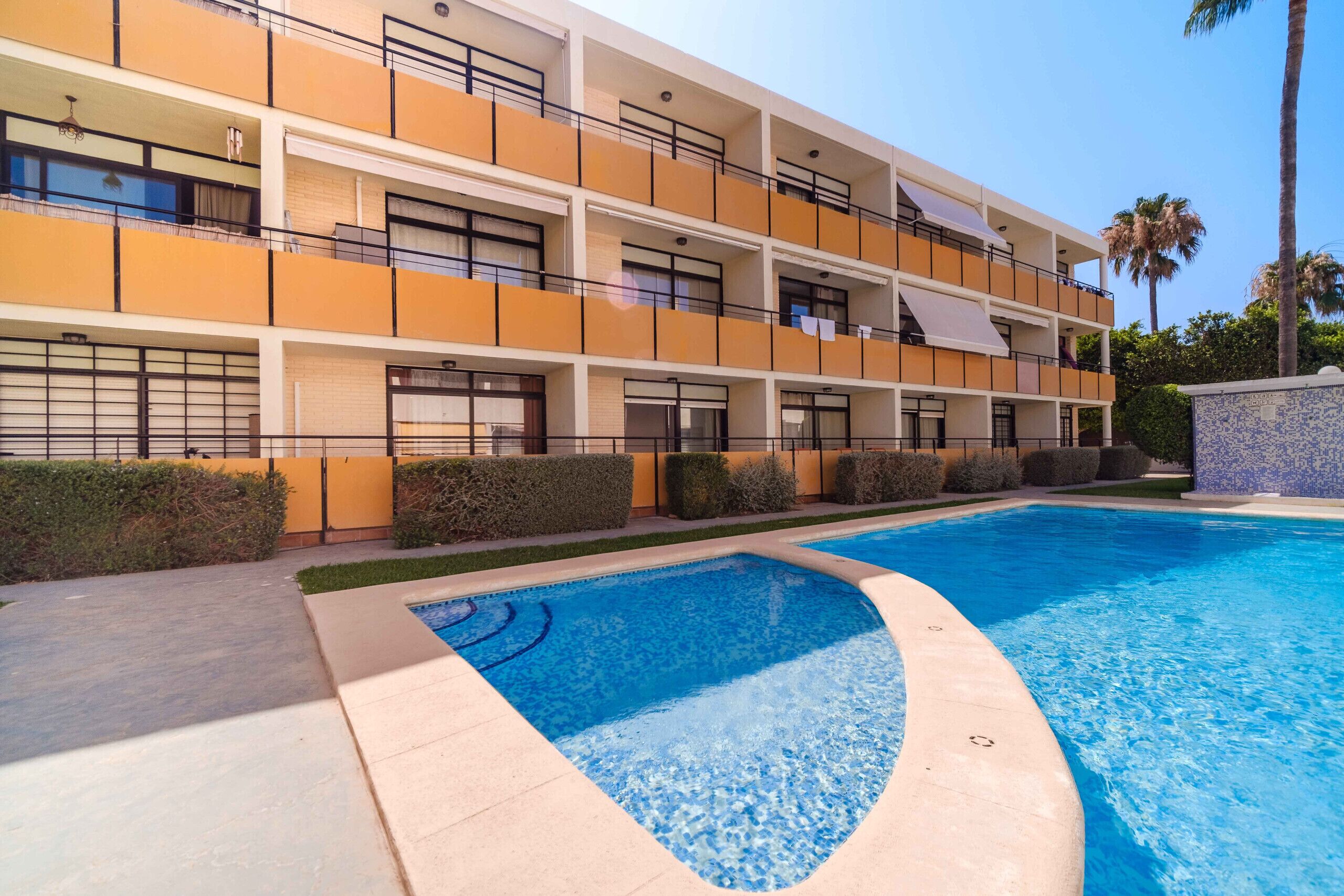 A multi-story hotel with balconies, a swimming pool, and a landscaped garden.