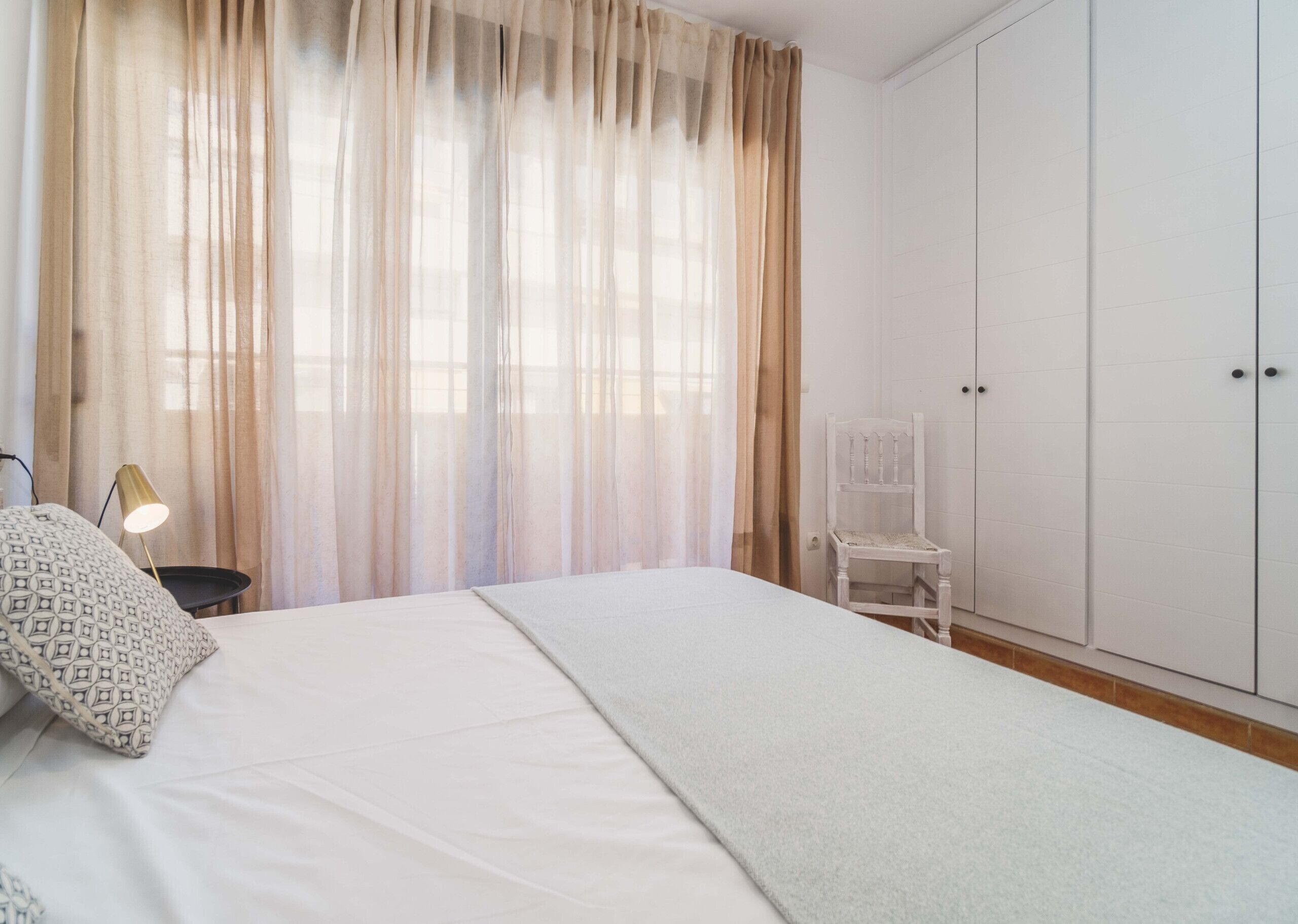 A bedroom with a bed, a chair, a lamp, and a wardrobe.