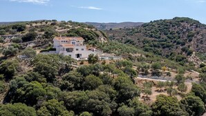 A white two-story house with a red-tiled roof, surrounded by dense greenery and hills in the background. - Villa Marietta by Estia (Hersonissos)