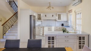 A modern kitchen with white cabinets, a marble island, and a staircase with black railings. - Villa Marietta by Estia (Hersonissos)