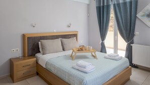 A neatly made bed with a light blue quilt, a wooden bedside table with a glass, and a tray with a plate and two cups. - Villa Marietta by Estia (Hersonissos)