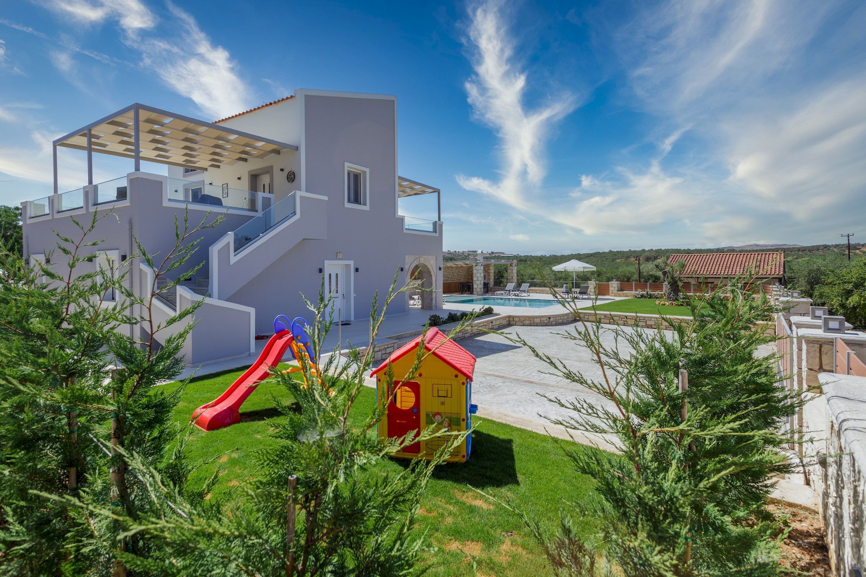 Un bâtiment moderne doté d’une piscine, d’un toboggan rouge et d’une petite maison de jeux.