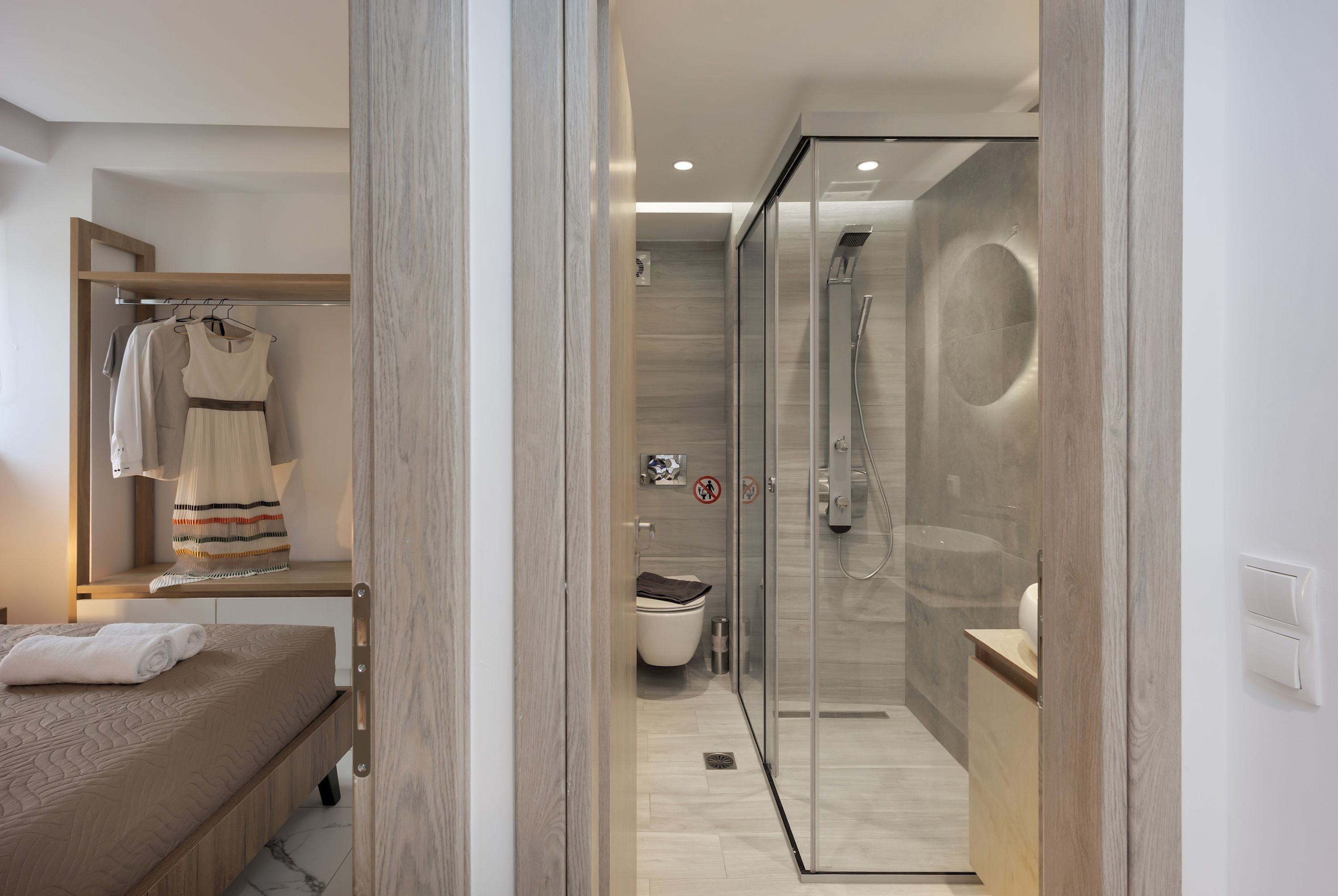 A modern hotel room with a bed, a walk-in closet, a glass-enclosed shower, and a toilet.