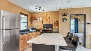 A modern kitchen with wooden paneling, stainless steel appliances, a marble island, and a dining area with leather chairs.