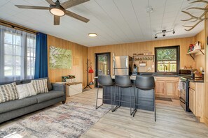 A modern kitchen with wooden cabinets, a refrigerator, and a bar area with stools. - Snowy Mountain Escape: Cozy Cabin & Hot Tub! (Bailey)