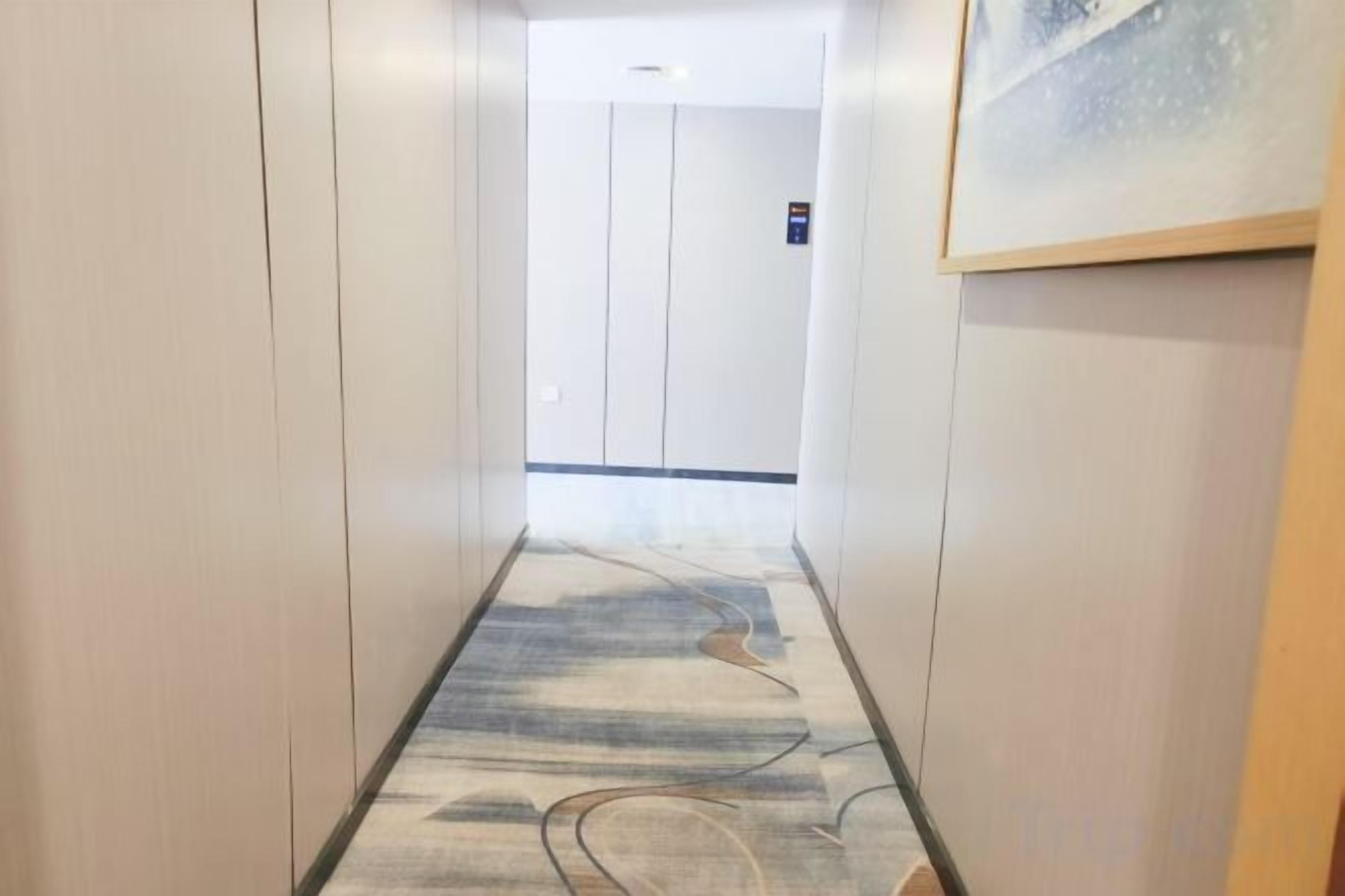 A hallway with a patterned floor, a door at the end, and a framed picture on the wall.
