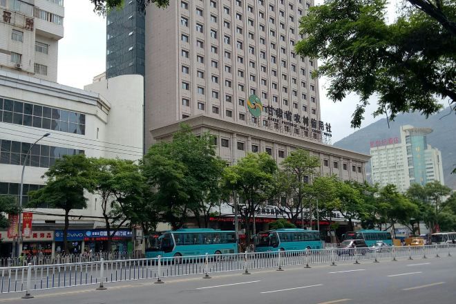 Un edificio de varios pisos con fachada plana, rodeado de árboles y una calle con autobuses estacionados.