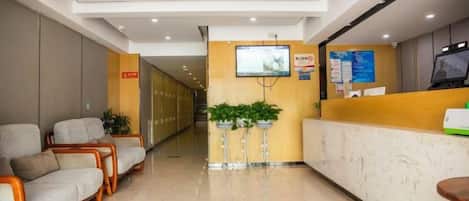 Zona de recepción de un hotel con mostrador, área de estar y un pasillo que conduce a las habitaciones.