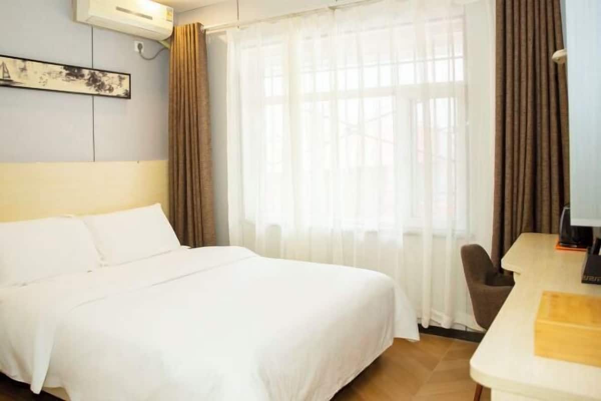 Quarto de hotel com cama, escrivaninha, cadeira e janela com cortinas.