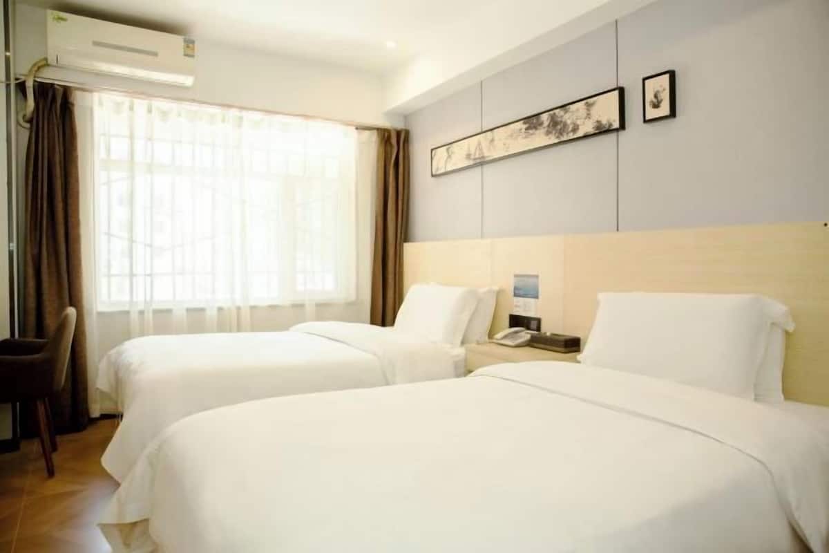Quarto de hotel com duas camas, uma escrivaninha com telefone e uma janela com cortinas.