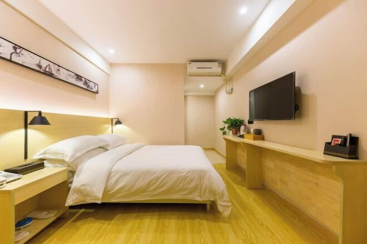 Quarto de hotel com cama, mesa de cabeceira, luminária, TV e pequena área de trabalho.