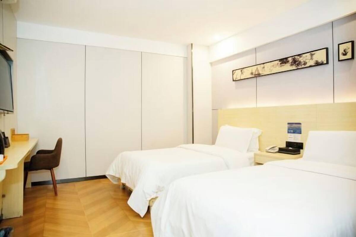 Quarto de hotel com duas camas, uma escrivaninha, uma cadeira e uma obra de arte na parede.