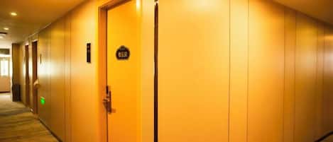 Un couloir d’hôtel avec une porte fermée, une enseigne au-dessus, et un sol recouvert de moquette.