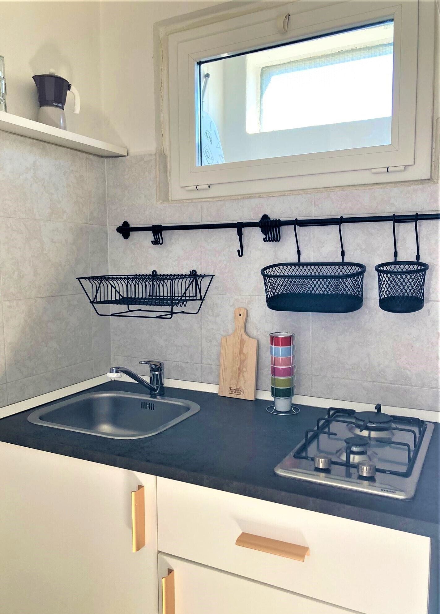 A kitchen with a black countertop, a gas stove, a sink, and hanging baskets on the wall.
