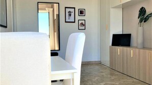 Una cocina moderna con armarios blancos, una mesa de comedor con sillas y un televisor sobre una estantería de madera.