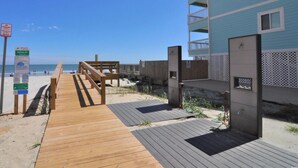 A wooden boardwalk leading to a beach with a blue building in the background.