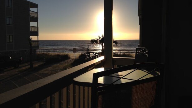 A balcony with a view of the ocean at sunset.