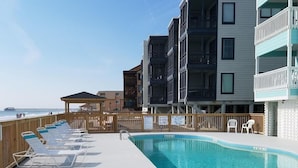 A pool area with lounge chairs, a wooden deck, and a view of a pier and buildings.