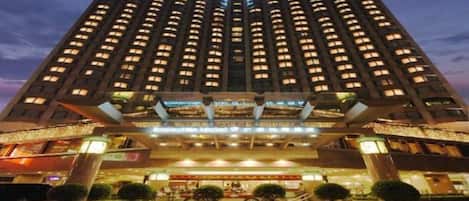 Un hotel moderno de gran altura con varios pisos, una entrada destacada y una fachada bien iluminada.