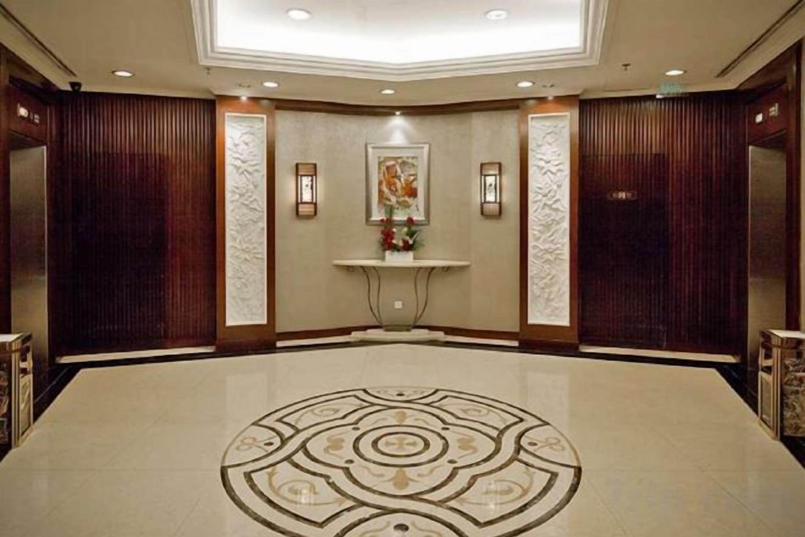 Un vestíbulo de hotel con un mostrador de recepción central, paneles decorativos en la pared y un diseño de piso estampado.