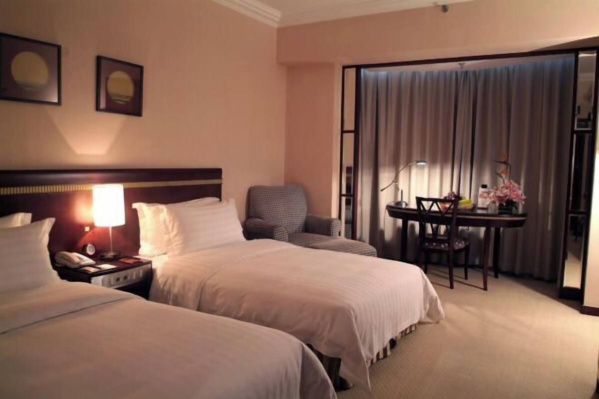A hotel room with two beds, a desk, a chair, a lamp, and a curtain.