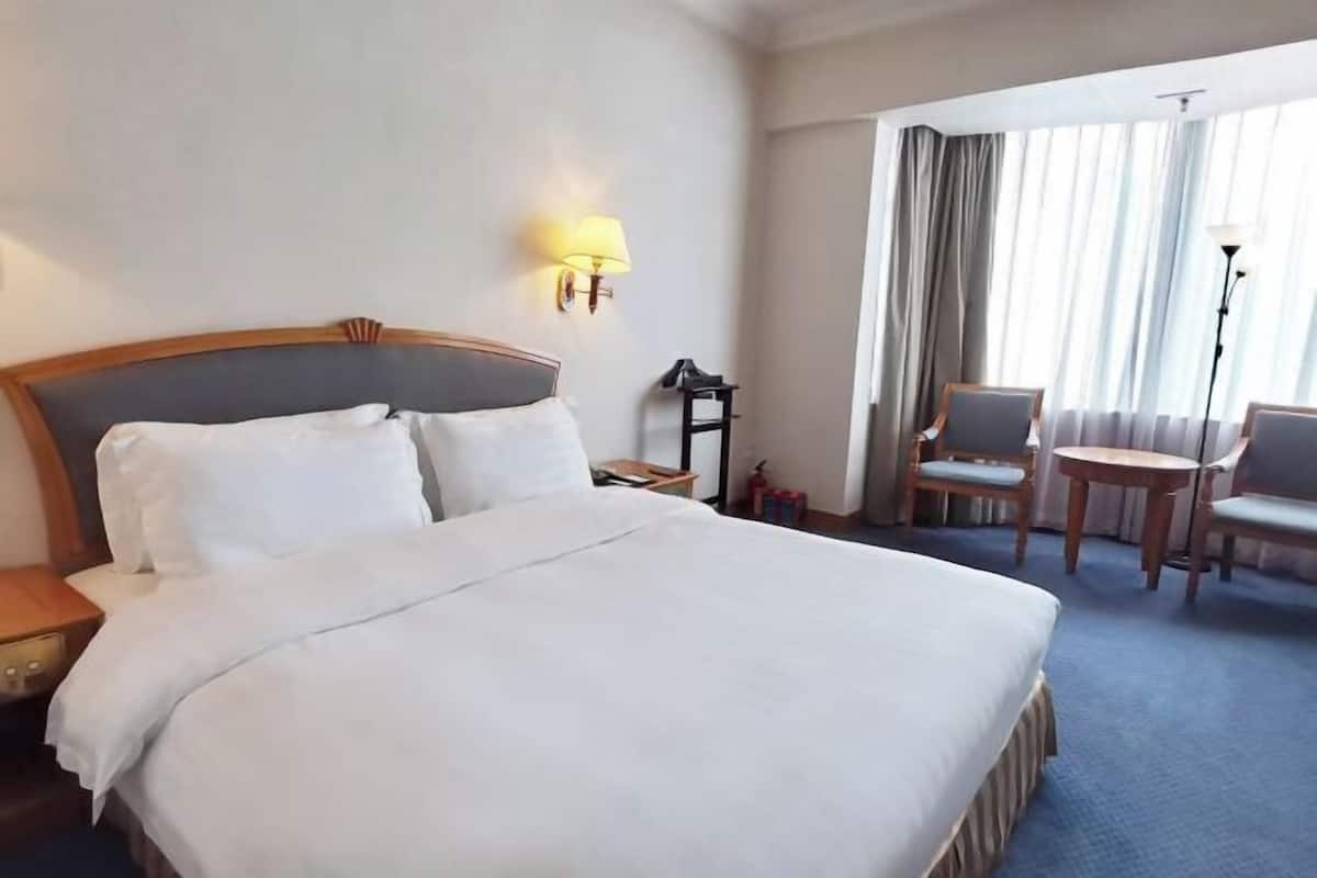 A hotel room with a large bed, a desk, two chairs, a lamp, and a view of the outdoors through the window.