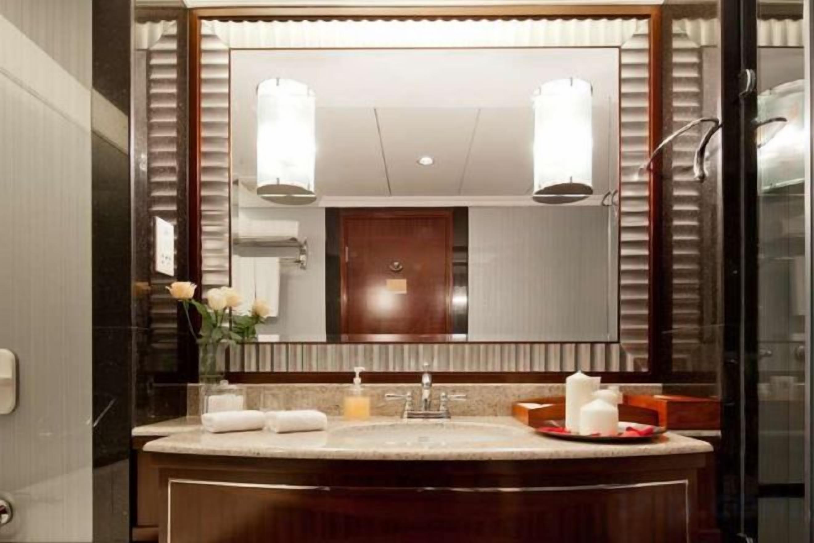 A bathroom with a large mirror, a sink with a towel, and a vase with flowers.
