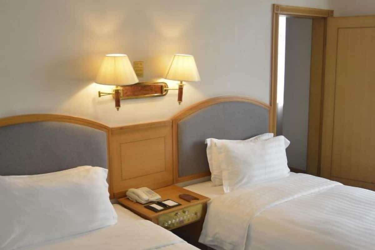 A hotel room with two beds, a nightstand with a lamp, a telephone, and a small table with a book and a wallet.