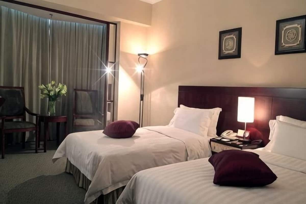 A hotel room with two beds, a desk, a chair, a lamp, and a window with curtains.