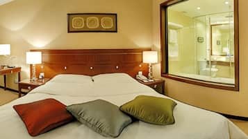 A hotel room with a large bed, bedside lamps, a mirror, and a view of the bathroom.