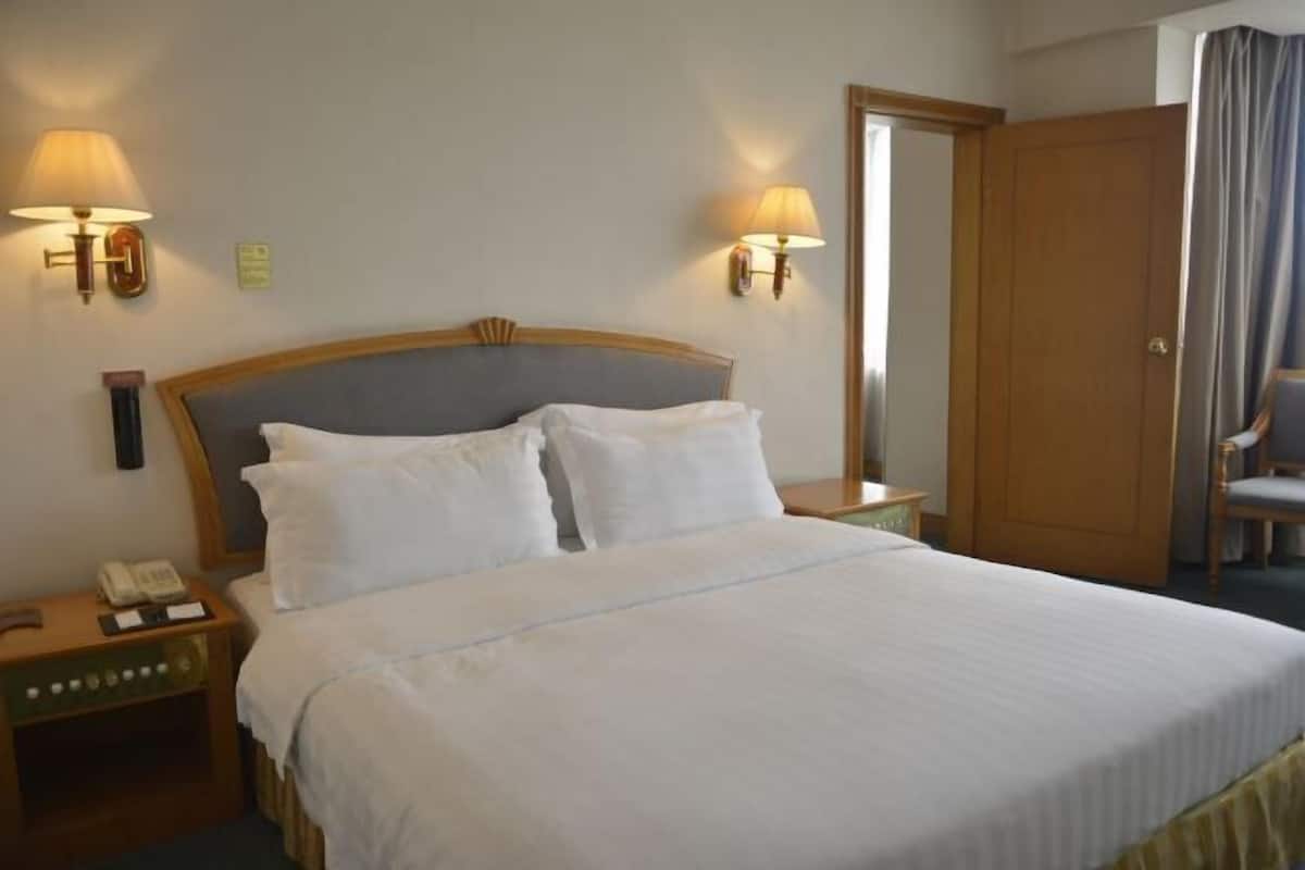 A hotel room with a large bed, two bedside lamps, a nightstand with a phone, and a mirror.