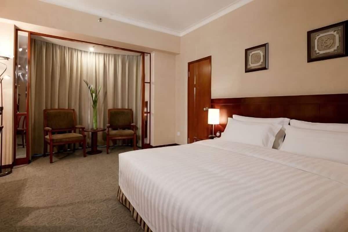 A hotel room with a bed, two chairs, a desk, a lamp, and a door.